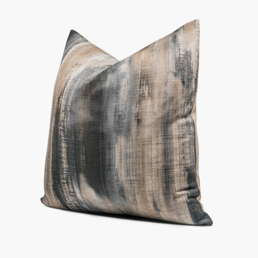 A linen-blend throw pillow with an abstract watercolor motif sits against a white background. The pillow includes shades of charcoal gray, steel blue, and beige. The pillow is shown from the side.