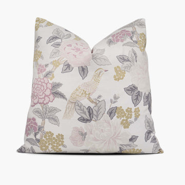 A throw pillow sits against a white background. The pillow has a bird and floral motif in pastel green and pink.