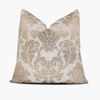 A champagne-beige damask throw pillow sits against a white background. The damask pattern is outlined in metallic-silver thread and set against a white, woven criss-cross base.