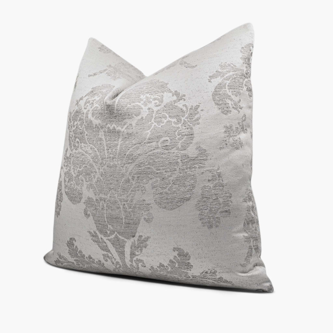 A silver gray throw pillow with a large-scale damask motif sits against a white background. The pillow is shown from the side.