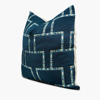 A dark blue, wool throw pillow is shown from the side. The pillow has an embroidered geometric motif in shades of blue, silver, and yellow.