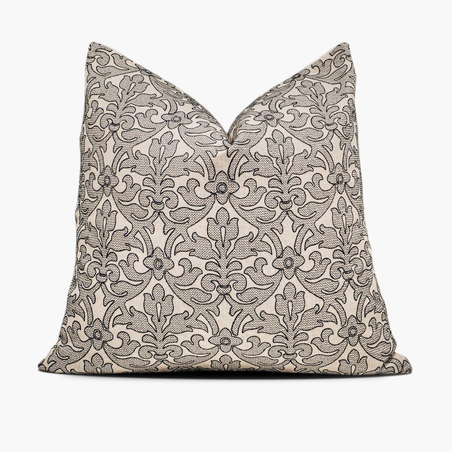 A tan throw pillow sits against a white background. The pillow has modern damask pattern embroidered in black.