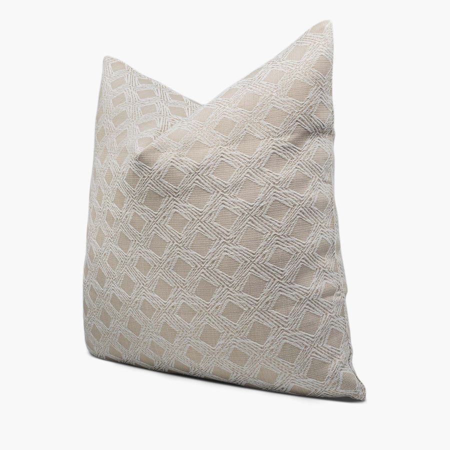 A beige throw pillow with a geometric diamond motif sits against a white background. The pillow is shown from the side.