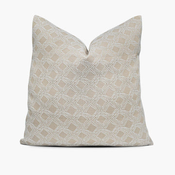 A beige throw pillow with a geometric diamond motif sits against a white background.