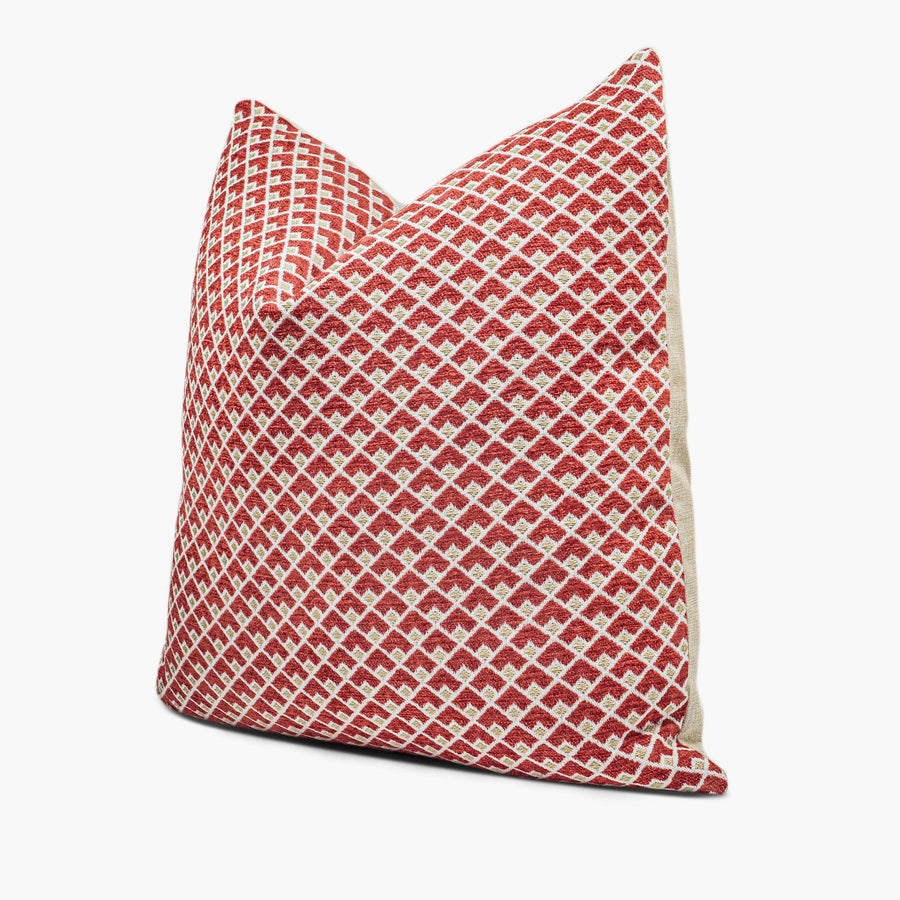 A ruby red and gold throw pillow with a geometric pattern sits against a white background. The pillow is shown from the side.