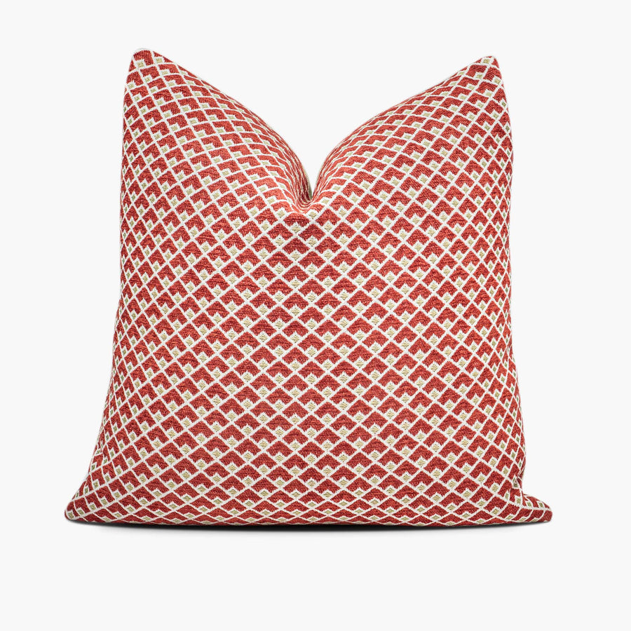 A ruby red and gold throw pillow with a geometric pattern sits against a white background.