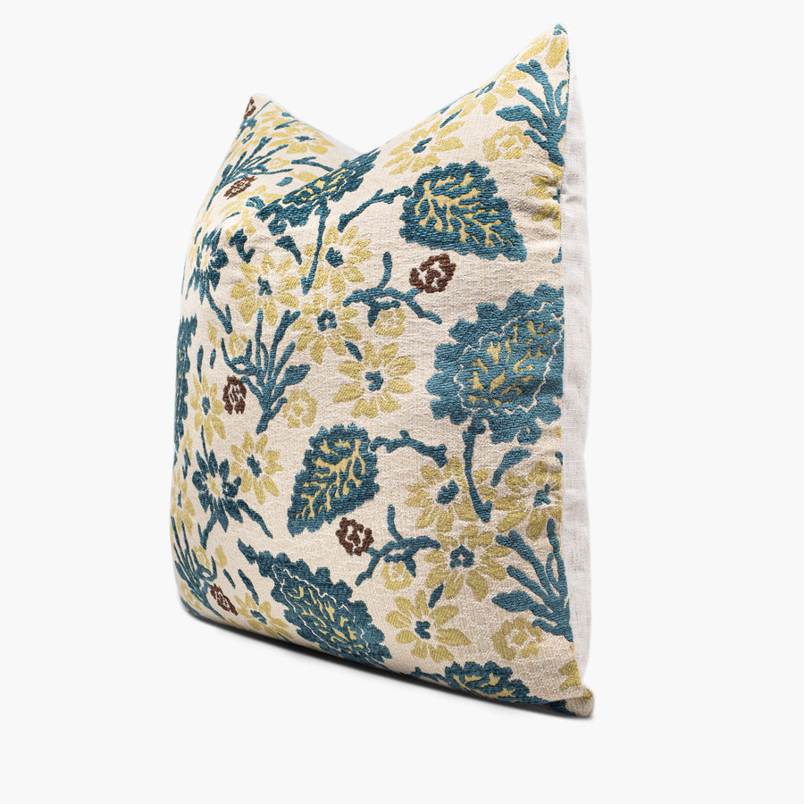 A chenille throw pillow with a floral motif is shown from the side. The motif features yellow flowers and teal leaves.